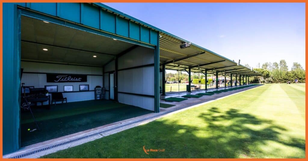 Vista de nuestras instalaciones de práctica premium en La Roca Golf, donde destacan los boxes techados con tecnología toptracer y trackman para el perfeccionamiento del swing. La imagen muestra nuestra zona de práctica diseñada con estándares profesionales, que combina espacios cubiertos para el entrenamiento técnico con una amplia zona de césped natural. El diseño modular y funcional refleja nuestro compromiso con el desarrollo integral del jugador amateur en un entorno de máxima calidad