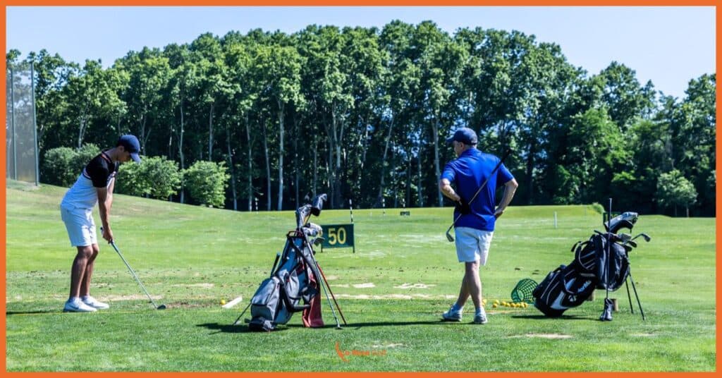 En nuestro campo de prácticas de La Roca Golf, dos jugadores perfeccionan su técnica en la zona de tiro de distancias. La imagen muestra la esencia de nuestro enfoque en el desarrollo del golf amateur: un espacio profesional con marcadores de distancia claramente visibles, donde nuestros jugadores practican con sus equipos completos en un entorno natural rodeado de vegetación mediterránea. Esta área técnica refleja nuestro compromiso con el aprendizaje progresivo y la mejora continua del juego.
