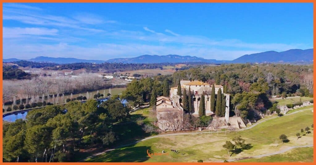 Vista aérea de la histórica masía de La Roca Golf, rodeada de cipreses centenarios, con los lagos del campo y el macizo del Montseny como telón de fondo. La imagen, tomada en invierno, muestra el fairway del hoyo 11 que se extiende junto a la masía, capturando la perfecta integración entre nuestro patrimonio arquitectónico y el diseño del campo de golf. La perspectiva aérea revela la ubicación estratégica de la edificación y su relevancia como punto de referencia en el recorrido.