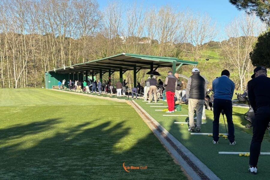 Nuevo Tee Line de La Roca Golf Barcelona con jugadores practicando en puestos cubiertos sobre césped artificial, rodeado de naturaleza y árboles en un centro de entrenamiento premium para mejorar tu swing en Cataluña