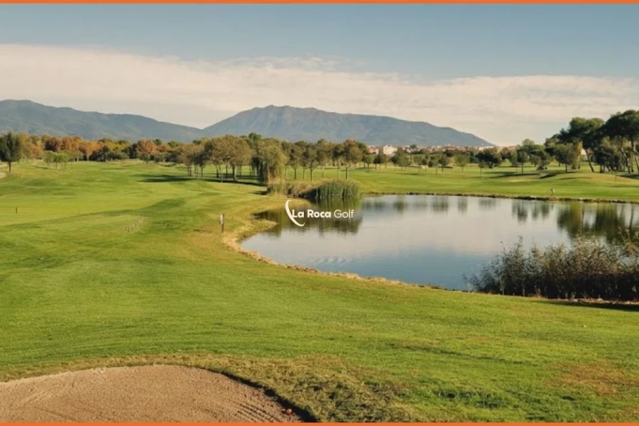 Campo de golf La Roca Golf con lago y green en primer plano, paisaje natural con el macizo del Montseny al fondo, día soleado.