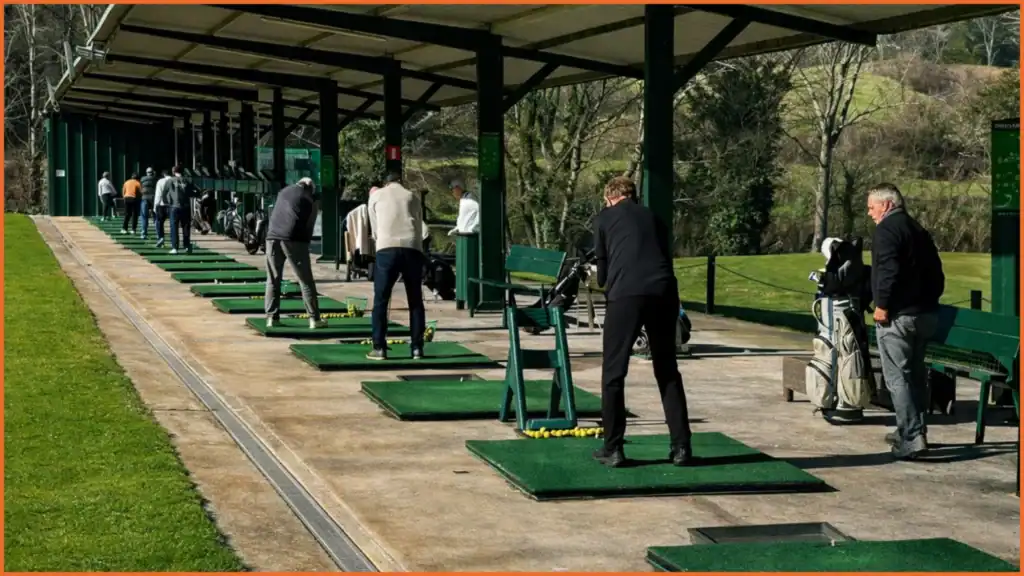 Varios jugadores practicando en el driving range cubierto de La Roca Golf, con alfombrillas verdes, bolas preparadas y un entorno natural cuidado con luz suave.