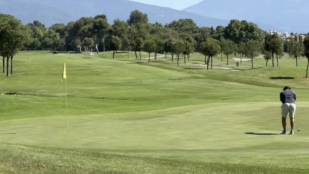 Golfista haciendo putt en un green de La Roca Golf con el campo y la montaña al fondo, cerca de Barcelona