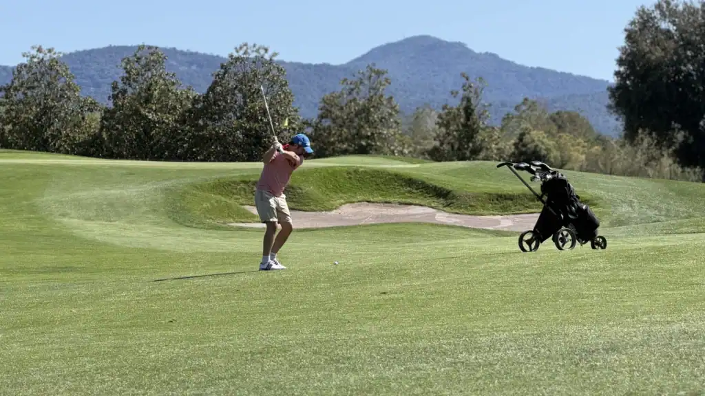 Golfista ejecutando un swing en La Roca Golf en un día soleado, con montaña al fondo, cerca de Barcelona