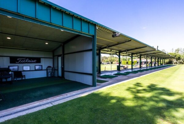 Línea de puestos cubiertos del Driving Range de La Roca Golf con los tees de césped artificial y el box de análisis
