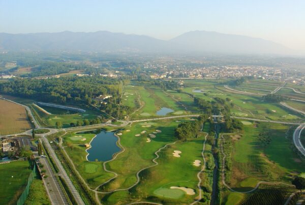 Vista aérea de La Roca Golf con el pueblo y las montañas al fondo, campo ideal para un fin de semana de golf en Barcelona