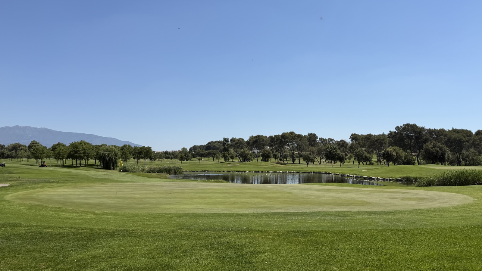 Green amb bandera groga i llac al darrere a La Roca Golf, exemple d'obstacle d'aigua