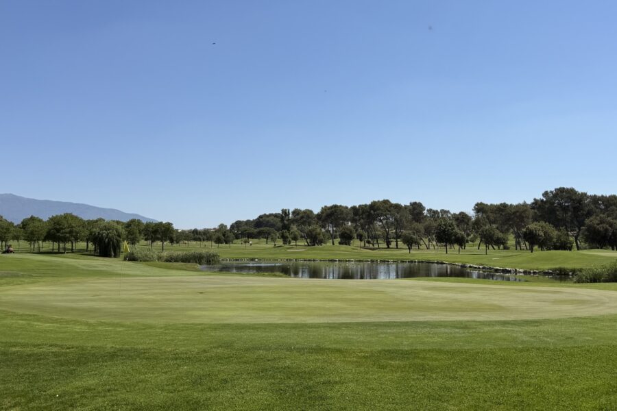 Green con bandera amarilla y lago detrás en La Roca Golf, ejemplo de obstáculo de agua
