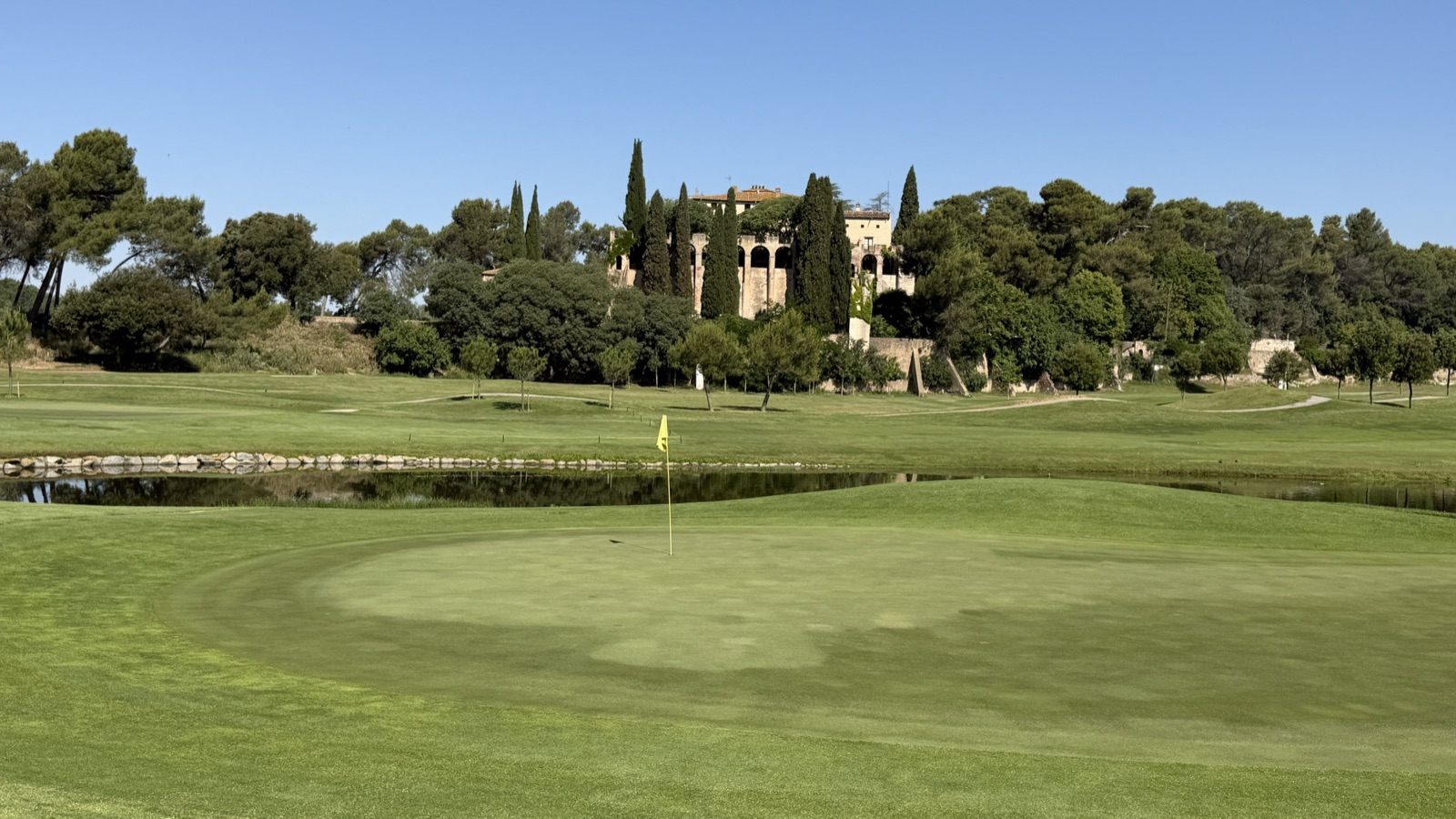 Green con lago de La Roca Golf en un día soleado de verano, ideal para el golf de mañana