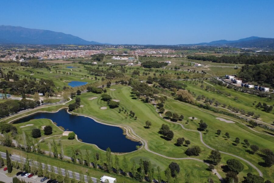 Vue aérienne de La Roca Golf avec ses lacs et la route d'accès, le village du Vallès Oriental et le massif du Montseny en arrière-plan