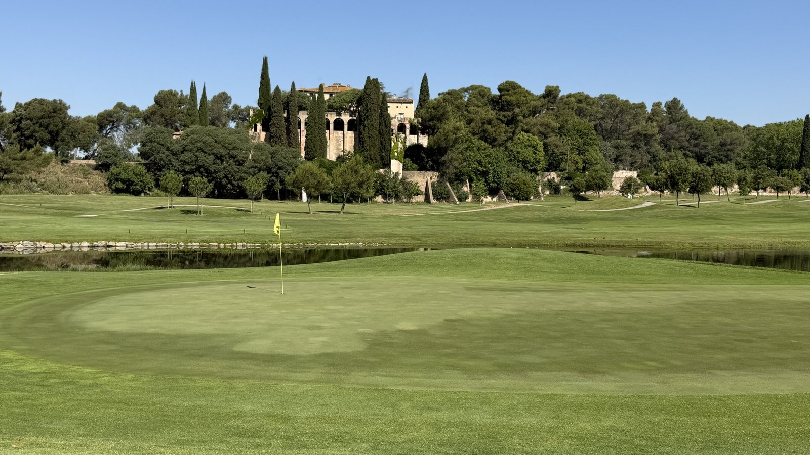 Green del hoyo 13 de La Roca Golf con el lago detrás y la masía al fondo