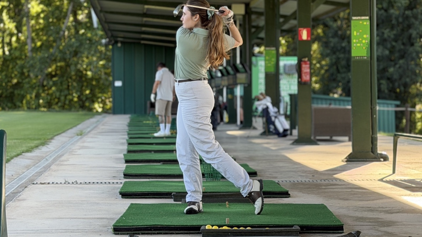 Golfeuse terminant son swing sous un poste couvert du practice de La Roca Golf, en fin d'après-midi.