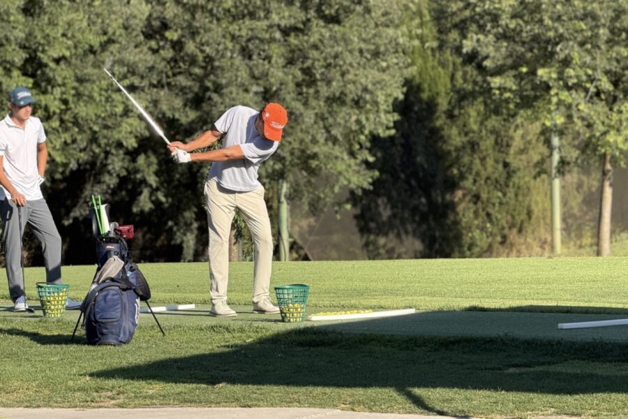 Golfer practising his swing on the Driving Range at La Roca Golf, with baskets of balls and another player watching.