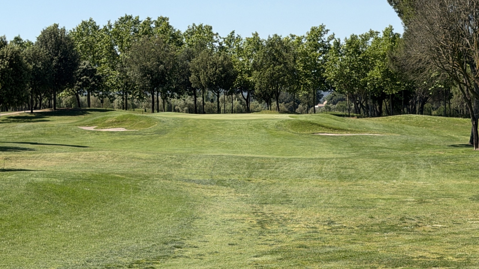 Green del hoyo 6 de La Roca Golf protegido por un bunker a cada lado, visto desde la calle.