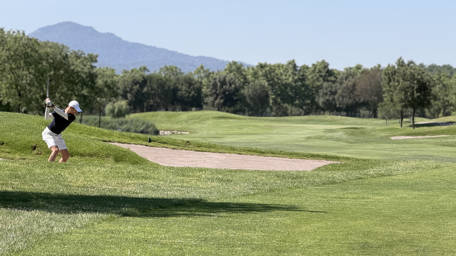 Jugador executant un cop des de l'herba alta al costat d'un bunker de carrer a La Roca Golf.