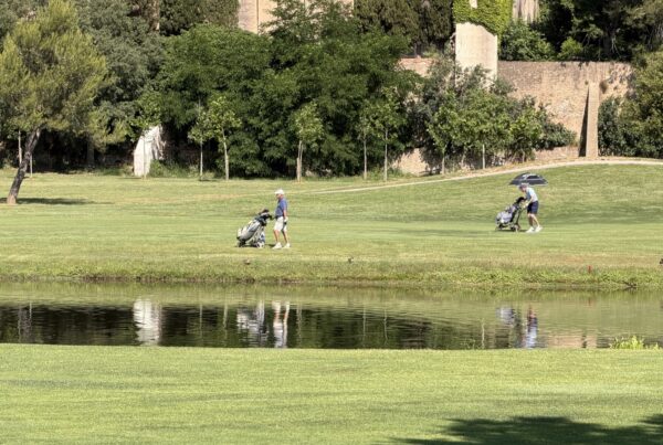 Deux joueurs marchant avec leur chariot manuel sur un fairway plat de La Roca Golf, au bord d'un des lacs du parcours.
