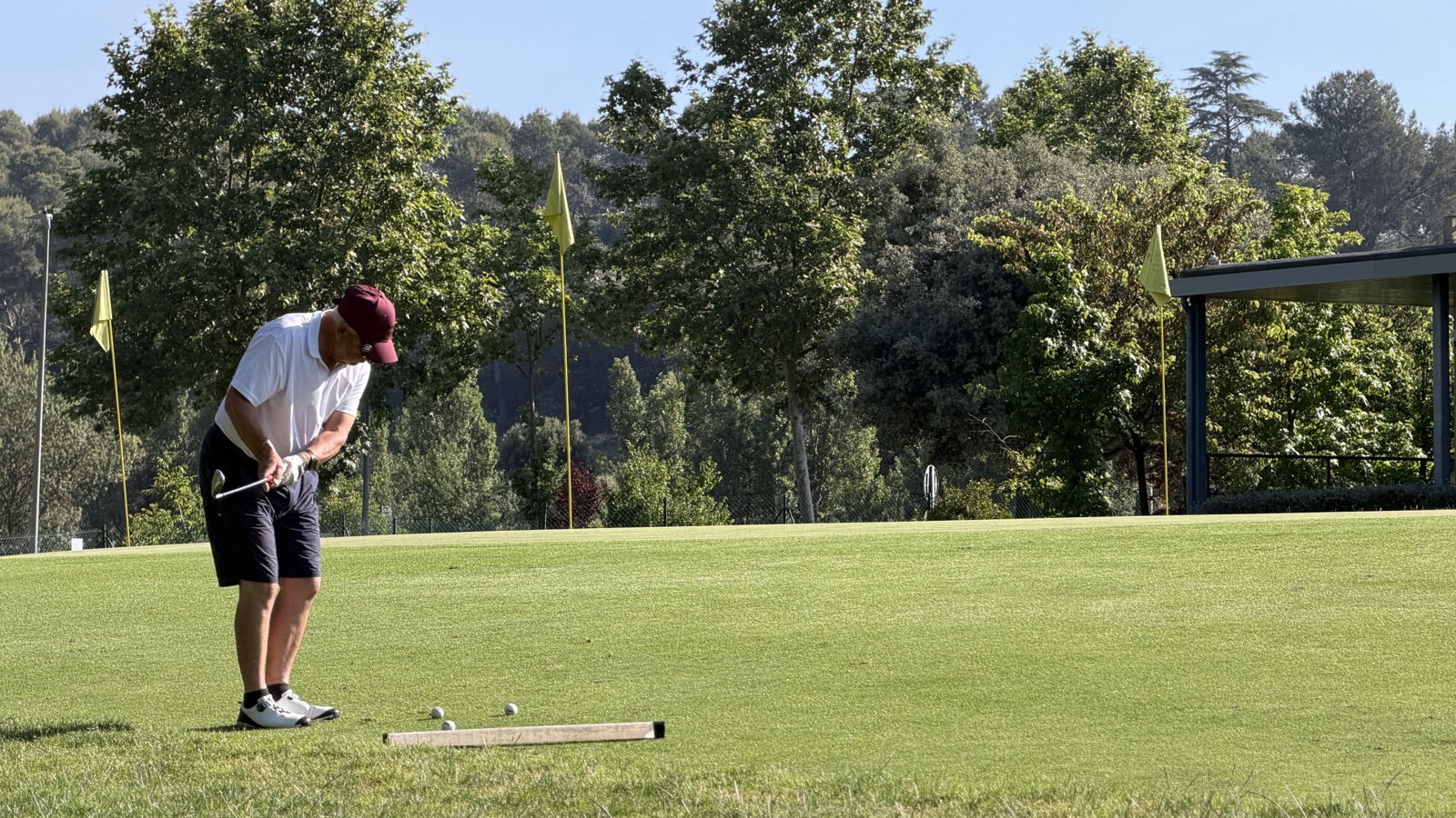 Jugador practicando golpes de approach hacia las banderas objetivo de la zona de juego corto de La Roca Golf, con una barra de alineación en el suelo.