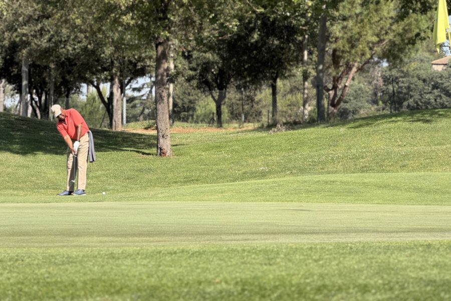 Jugador ejecutando un putt en un green de La Roca Golf con la bandera amarilla a la derecha.